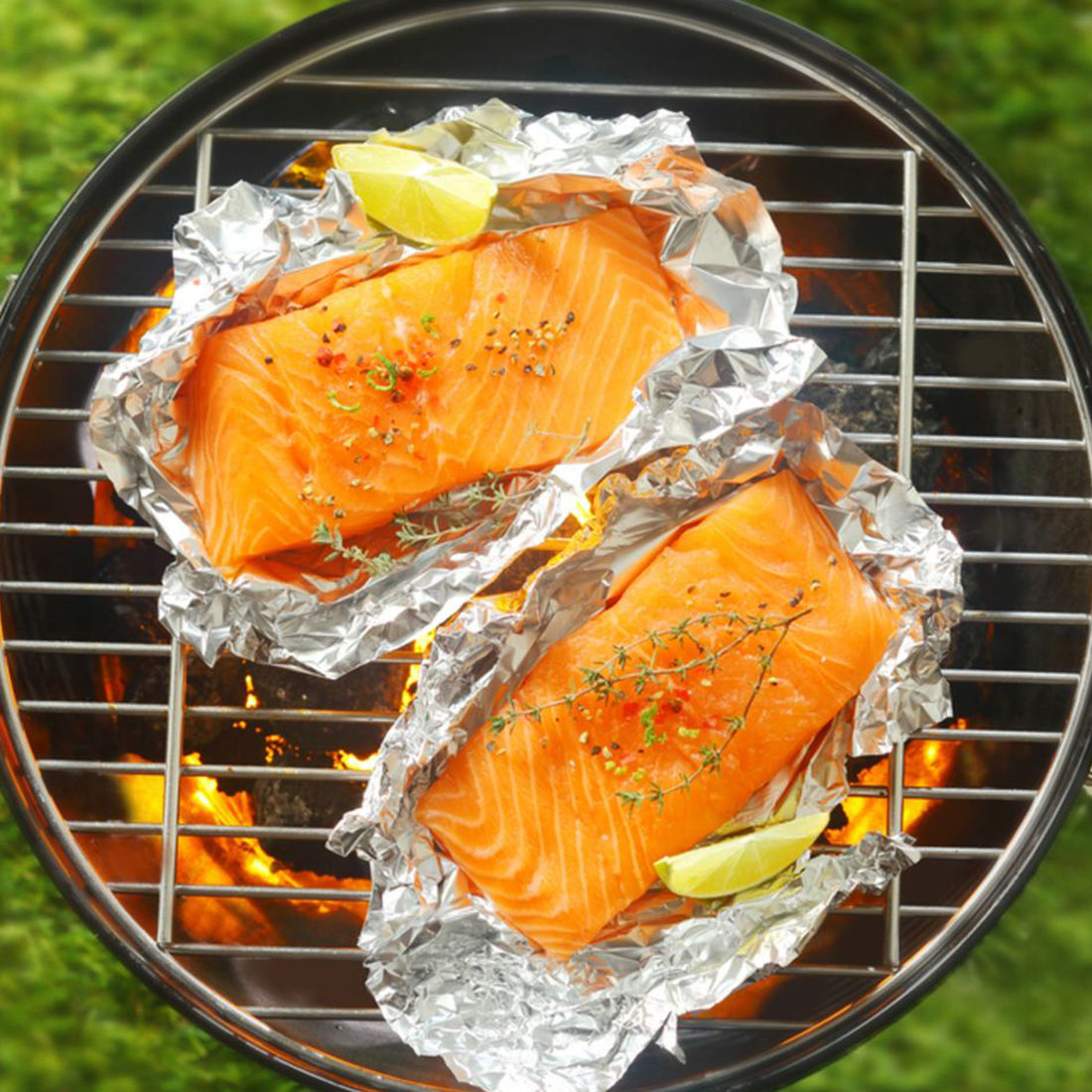 Salmon fillets in foil on a grill with lemon wedges